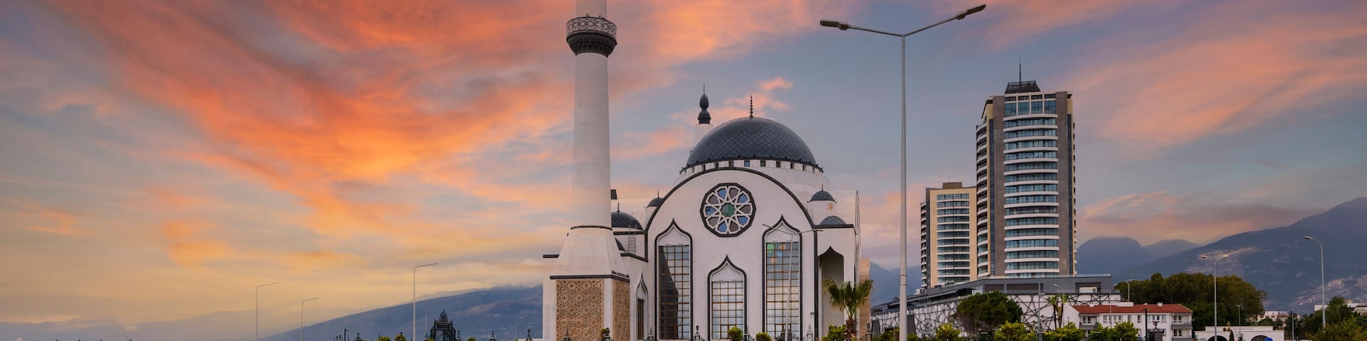 A mosque with a minaret, a modern building, and a coastal view.