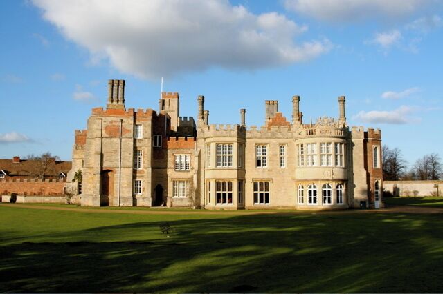 A large stone building with multiple chimneys and windows, surrounded by a well-maintained lawn.