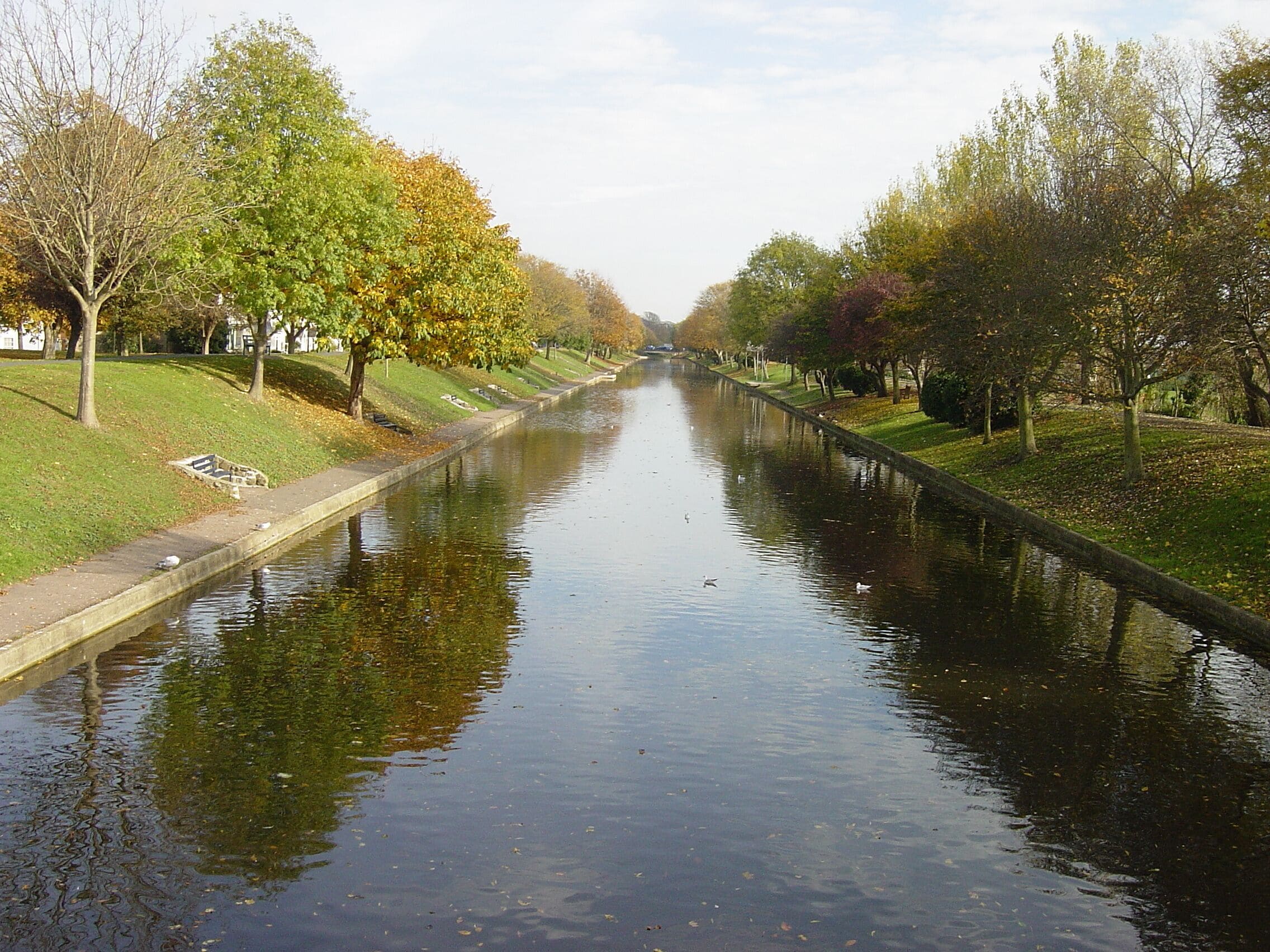 A calm canal flanked by trees and grassy banks.