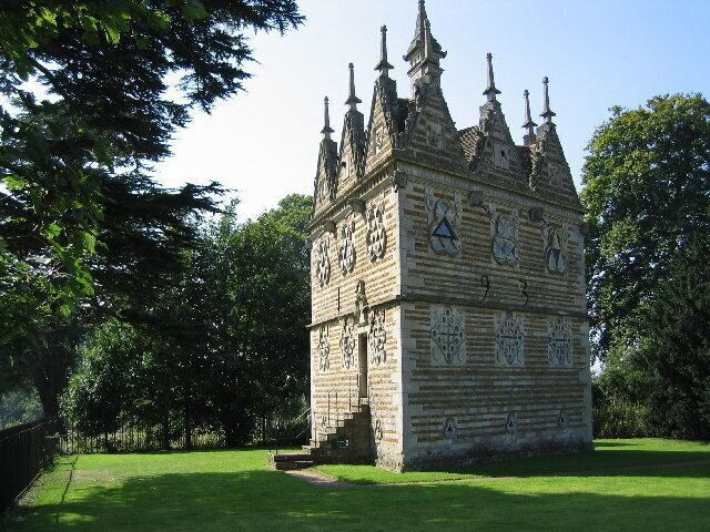 A historic tower with intricate stonework and multiple spires, surrounded by lush greenery.