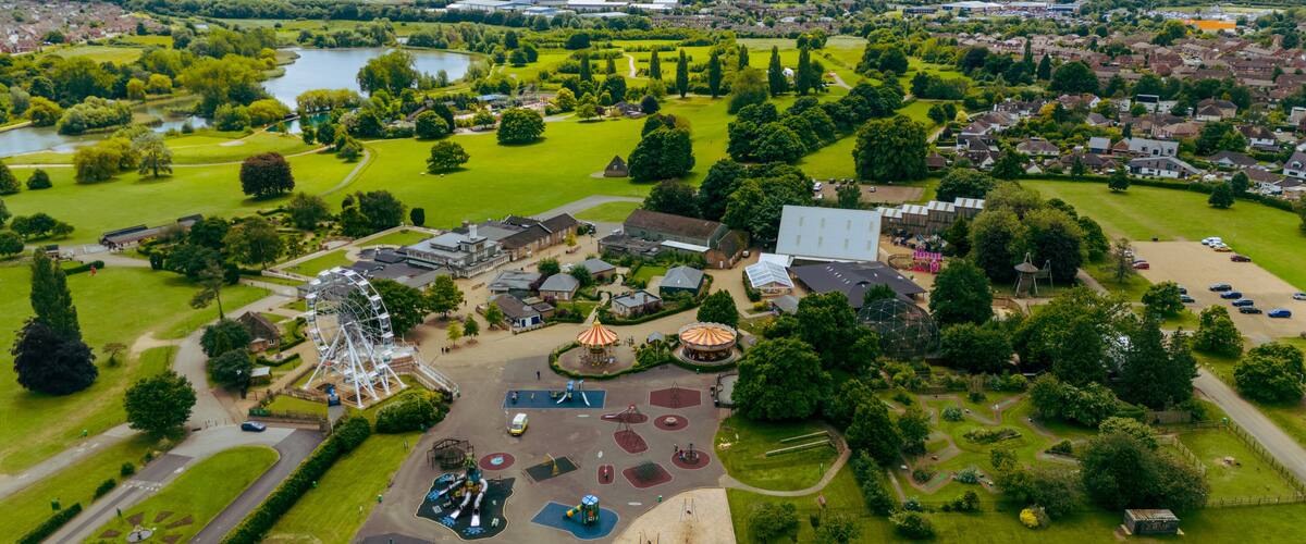 An aerial view of a park with a Ferris wheel, playgrounds, and a large building.