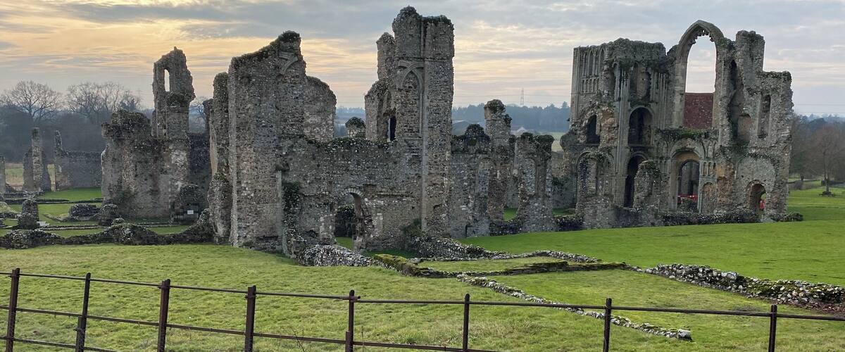A historic stone ruin with arches and towers, surrounded by a grassy field and a metal fence.