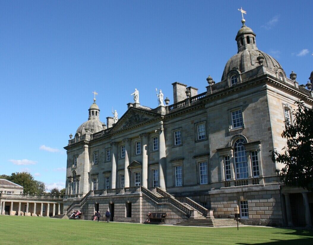A large stately building with multiple domes and columns, a well-manicured lawn, and a clear blue sky.