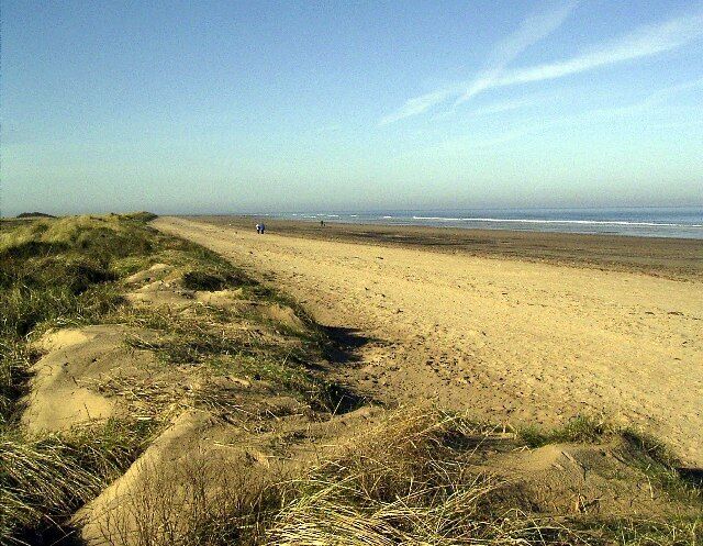 A sandy beach with dunes and the ocean in the background.