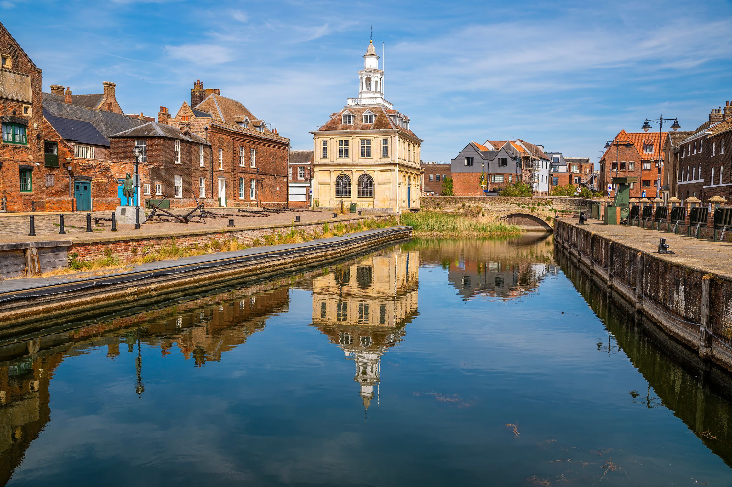 A canal with a reflection of buildings, a bridge, and a tower.