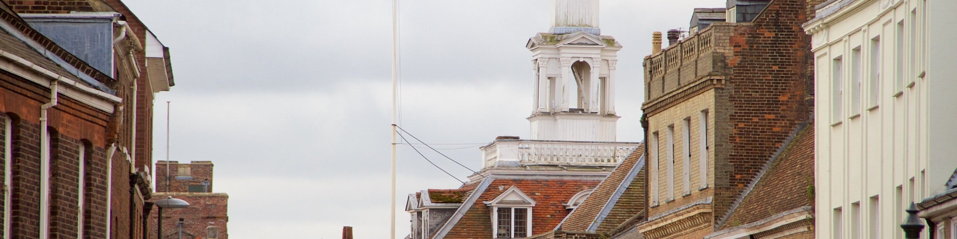 A historic street with traditional architecture, including a prominent church steeple and a flagpole.