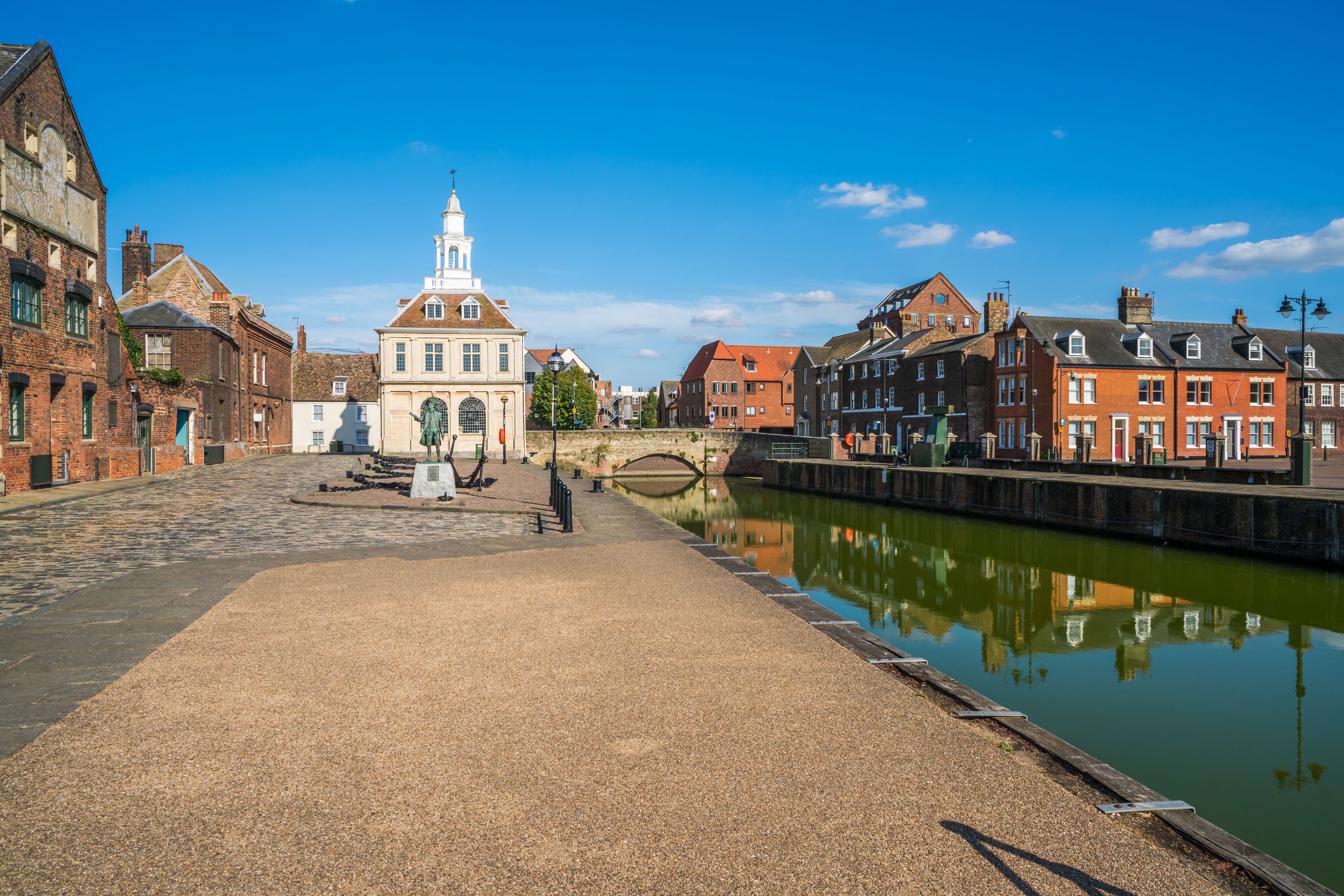 A cobblestone square with historic buildings, a canal, and a bridge.