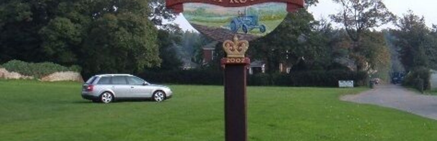 A signpost with 'North Runcott' written on it, set against a grassy field with a car in the background.