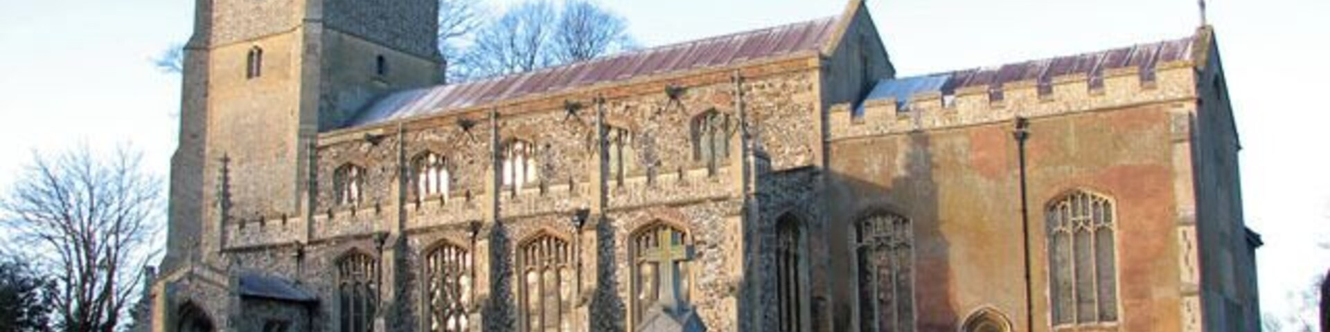 St Martin's church illuminated by winter sunlight. The war memorial can be seen in the foreground. St Martin > 1636596 is one of formerly two churches in the village of Fincham. St Michael's church (abandoned in 1745 after the collapse of its tower) used to be situated about 200 metres to the west and after it was pulled down some of it was used to repair St Martin. The church sits on an elevation north of High Street, the main thoroughfare through the village. The building dates mainly from the 15th century but was restored in the mid to late 1800s when the south porch was added. The stained glass windows > 1636627 date from that time also. The vestry on the north side dates from around 1503 and has an extra room above for the use of an assistant priest. The rood screen with its elaborately carved tracery and original painted decoration on the panels > 1636640 is C15. The most notable feature of the church is the magnificent Norman font > 1636645 which came from St Michael's church. It is only one of 13 square Norman fonts that still survive in north-west Norfolk and one of only three which have figures carved on the sides of the bowl. Six boards dating from 1717 and inscribed with texts from the Bible > 1636606 hang on the nave walls. The pulpit and pews were installed in Victorian times.