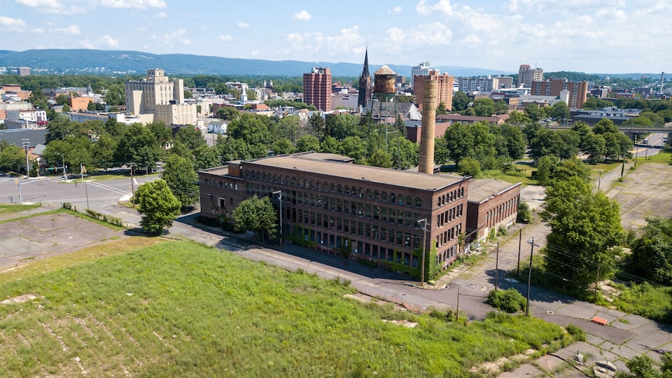 An industrial building with a tall chimney, surrounded by trees and urban buildings.