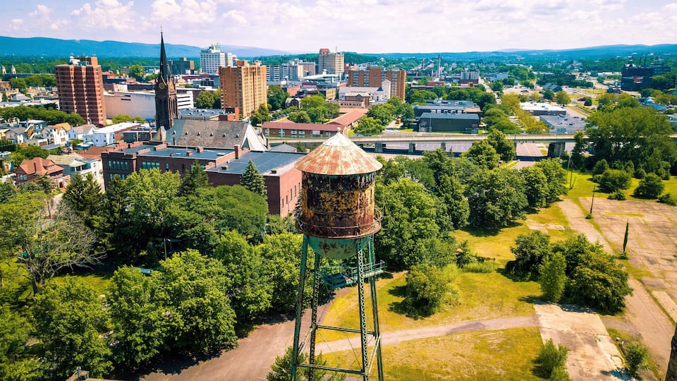 A cityscape with a prominent water tower, dense greenery, and various buildings.