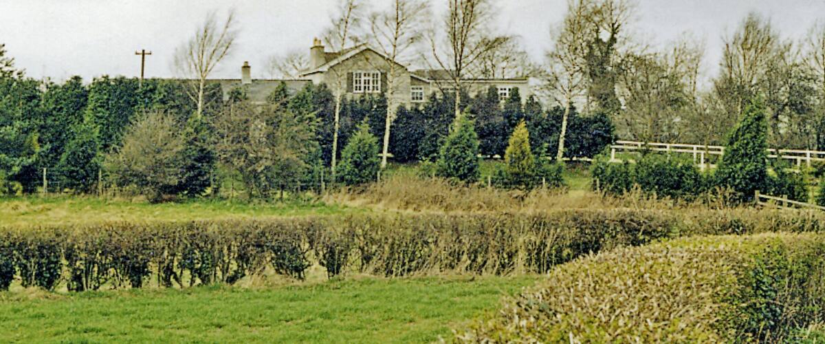 A large house surrounded by trees and a hedge.