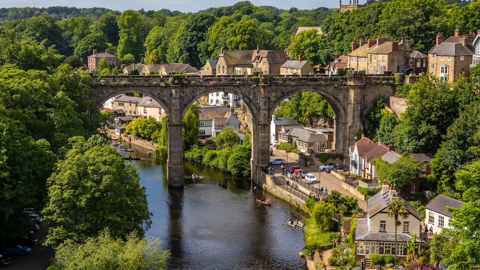A stone bridge over a river in a town surrounded by lush greenery.