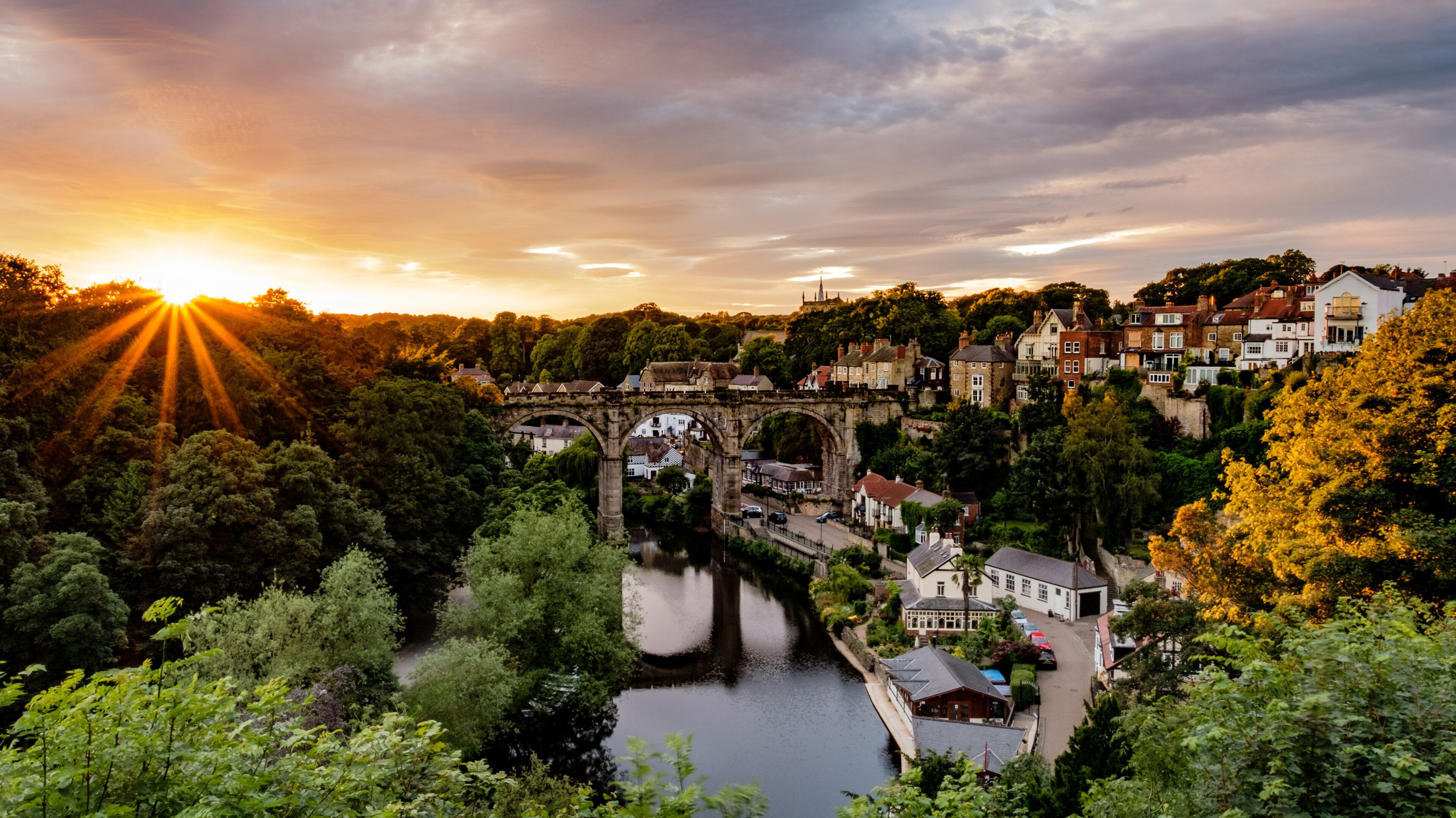 A historic stone bridge over a river, surrounded by lush greenery and traditional buildings.