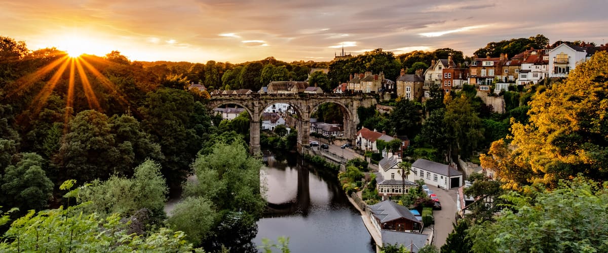 A historic stone bridge over a river, surrounded by lush greenery and traditional buildings.