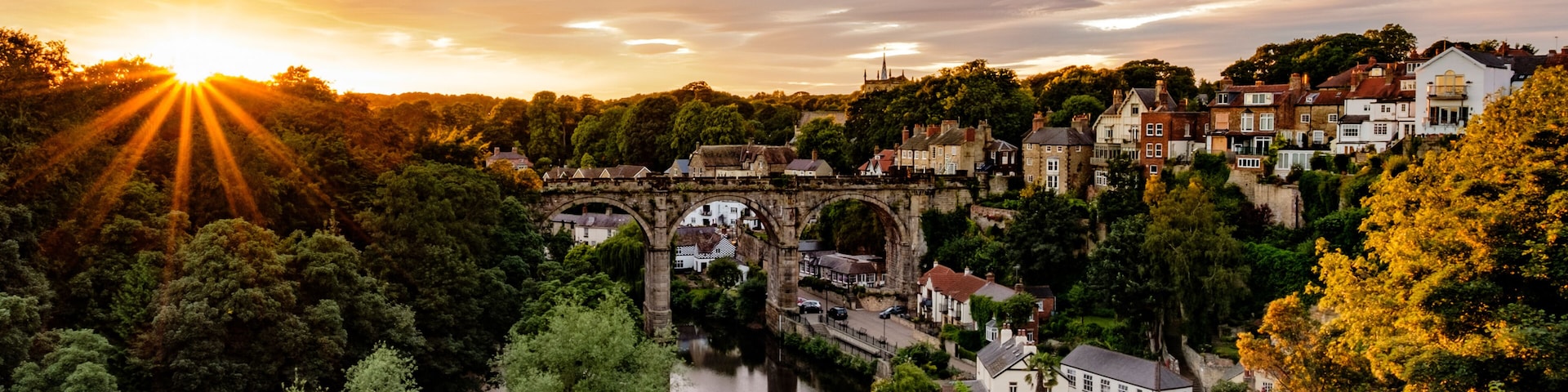 A historic stone bridge over a river, surrounded by lush greenery and traditional buildings.