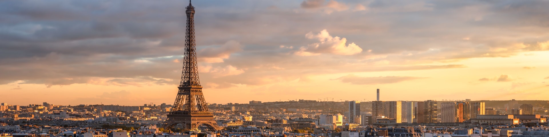 A Torre Eiffel em Paris com uma paisagem urbana ao fundo durante o pôr do sol.