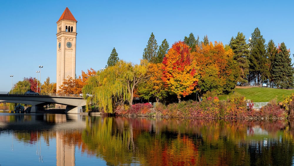 Un pont enjambant une rivière paisible, des arbres d’automne aux couleurs éclatantes et un clocher.