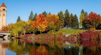 A bridge over a calm river, autumn trees with vibrant foliage, and a clock tower.