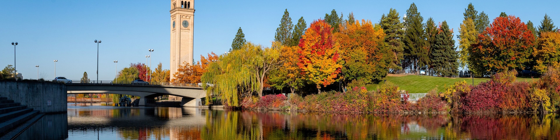 Uma ponte sobre um rio calmo, árvores de outono com folhagem vibrante e uma torre do relógio.