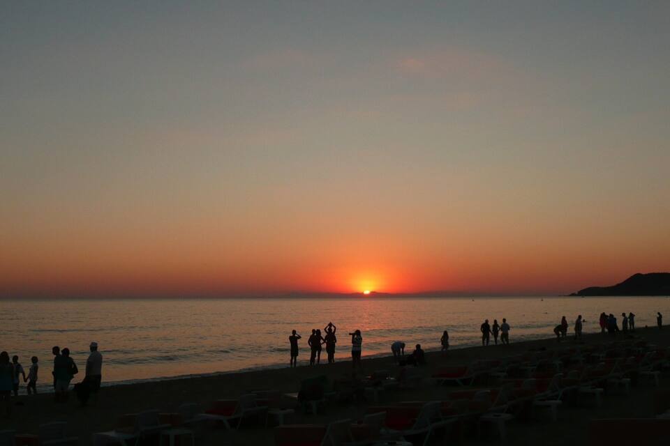 Un atardecer sobre una playa con gente y personas tomando el sol.