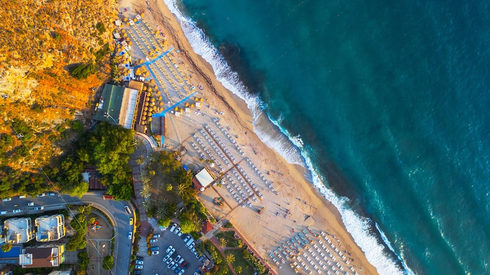 An aerial view of a coastal area with a beach, parking lots, and adjacent buildings.