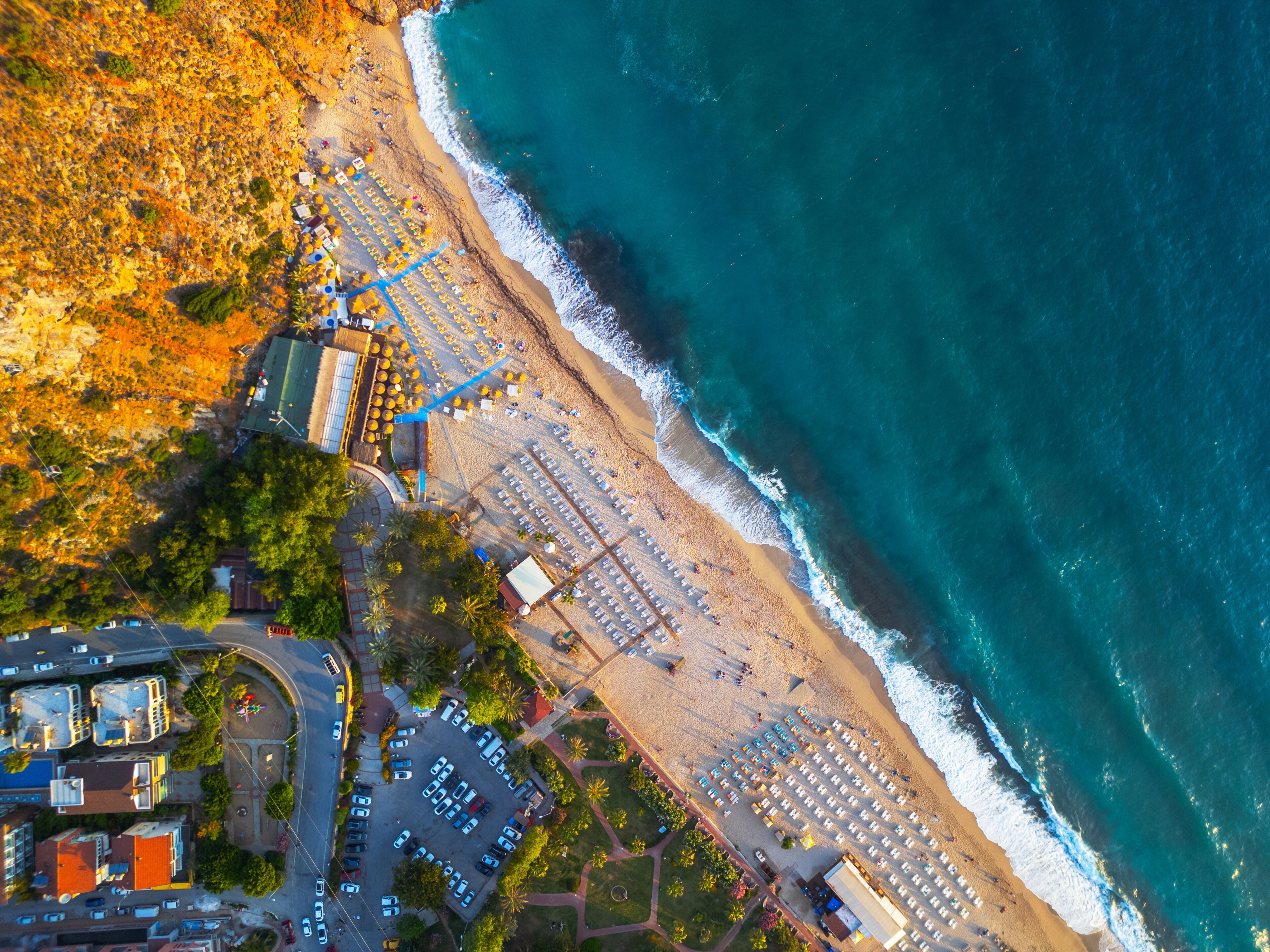 An aerial view of a coastal area with a beach, parking lots, and adjacent buildings.
