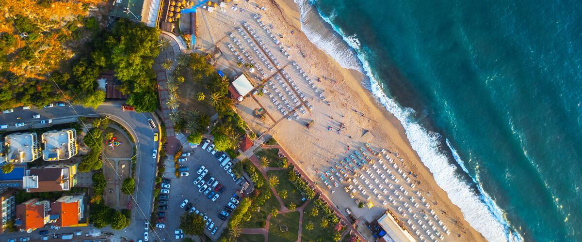 An aerial view of a coastal area with a beach, parking lots, and adjacent buildings.