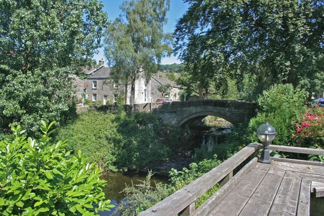 A stone bridge over a river, surrounded by lush greenery and a wooden walkway.