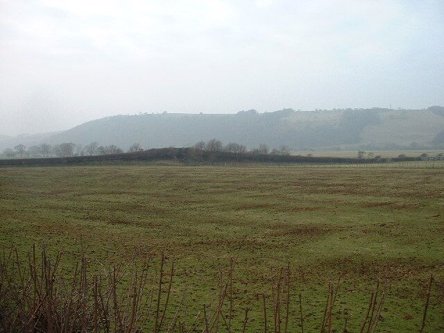 A flat, open field with sparse vegetation and distant hills.
