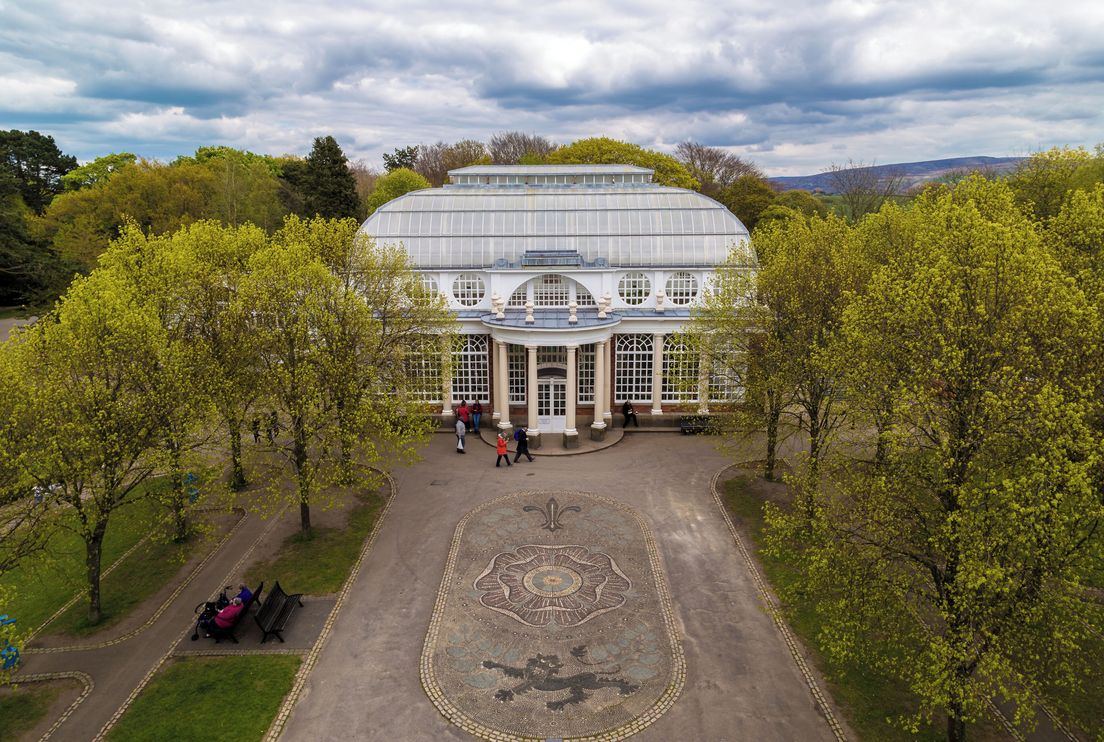 A large glass conservatory with a central dome and a decorative pavement.