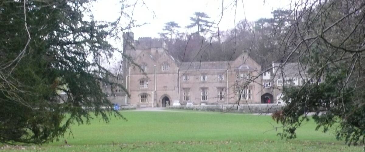 A large building with a central archway, surrounded by a grassy field and trees.