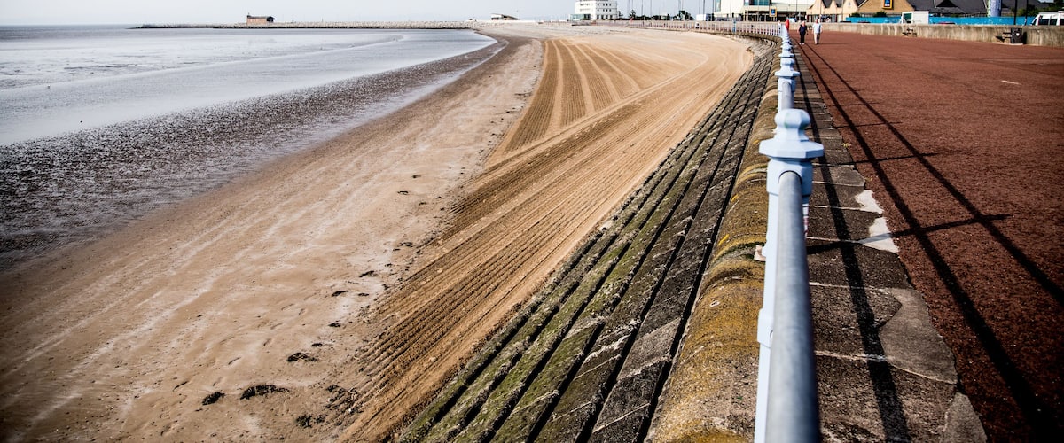A sandy beach with a metal railing and a building in the background.