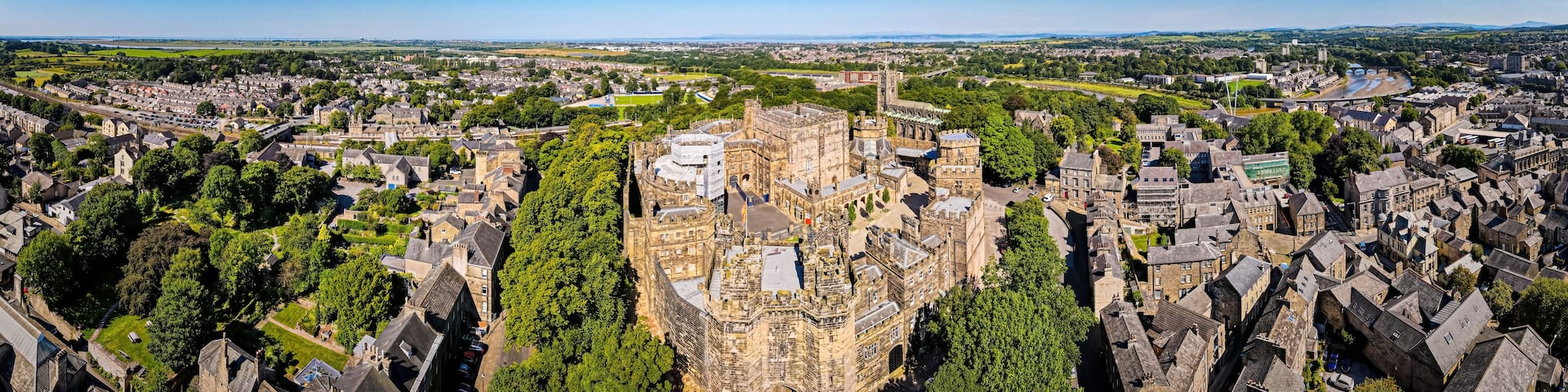 An aerial view of a historic town with a prominent castle, dense residential areas, and a river.