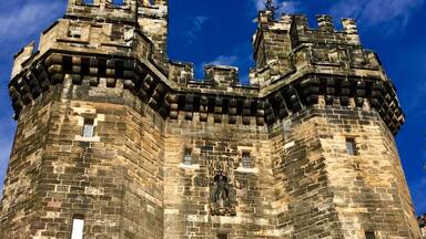 A historic stone castle with a large arched entrance, battlements, and a flag on top.