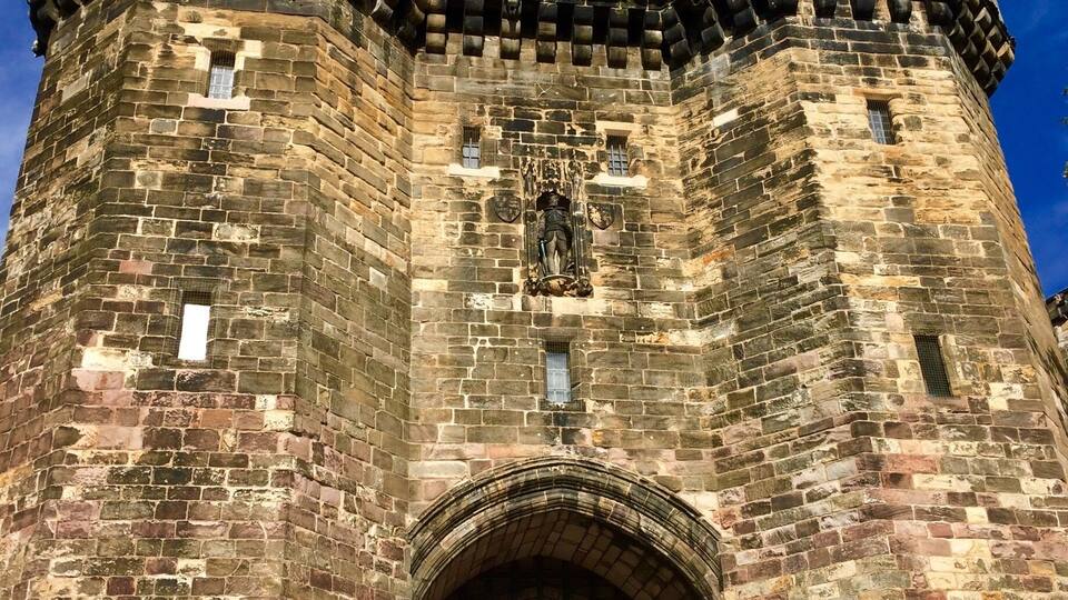 A historic stone castle with a large arched entrance, battlements, and a flag on top.
