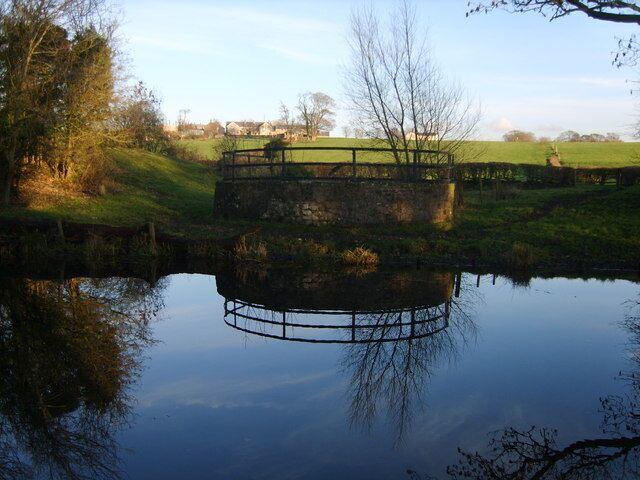 A circular stone bridge over a calm river, surrounded by grassy fields and trees.