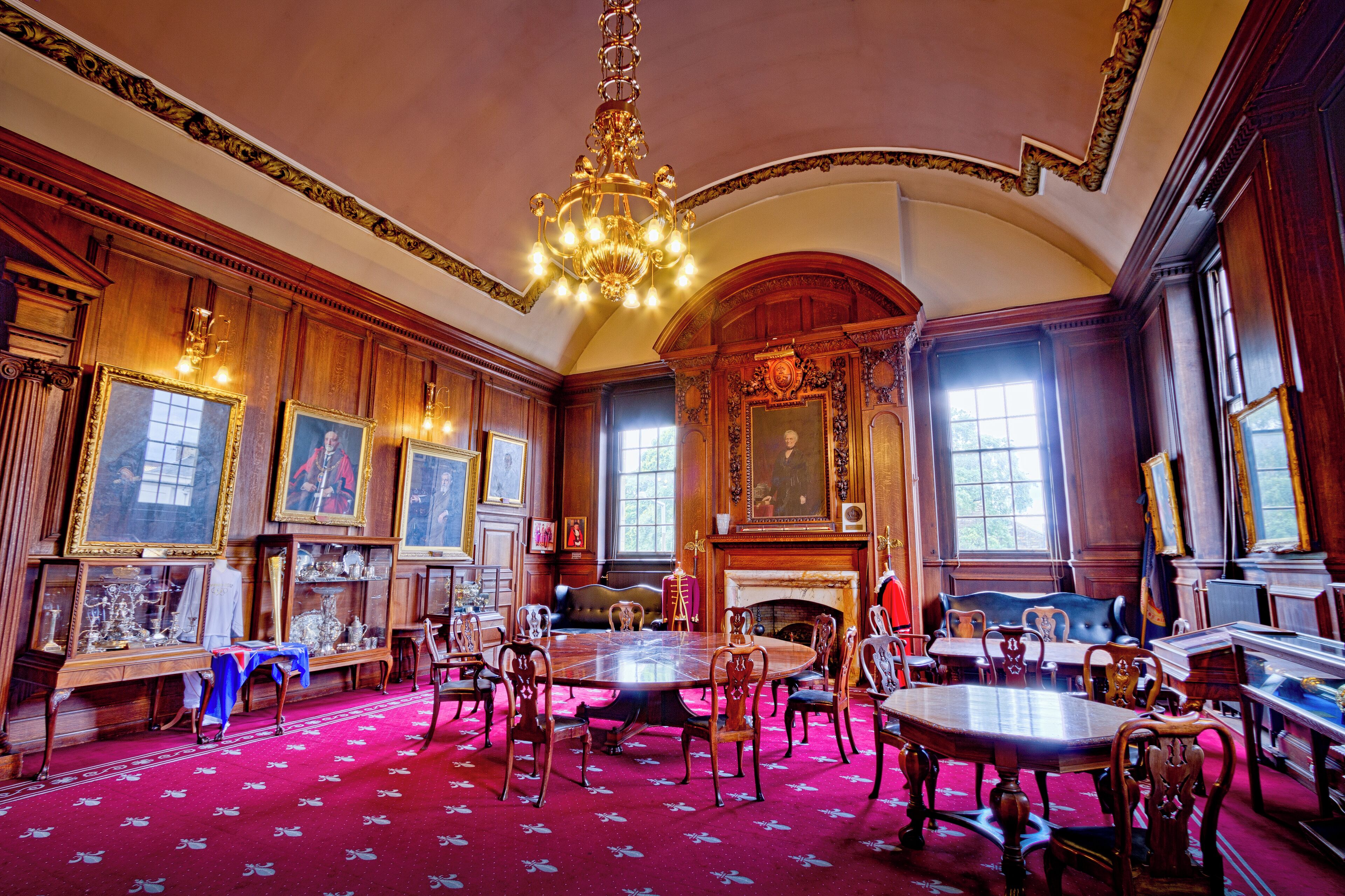 An ornate room with a large chandelier, wooden paneling, and a fireplace.