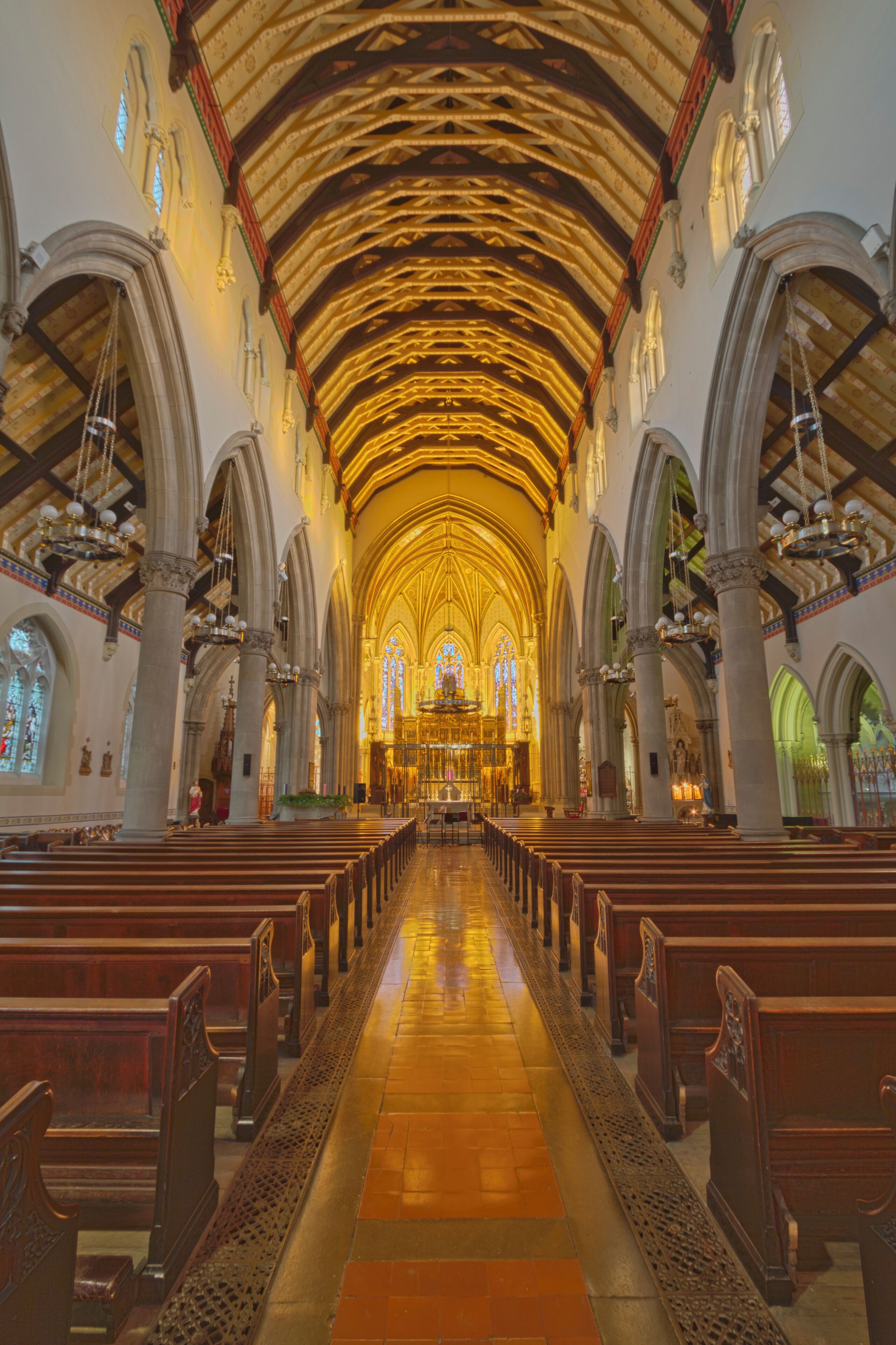 An interior of a church with wooden pews, a high vaulted ceiling, and stained glass windows.