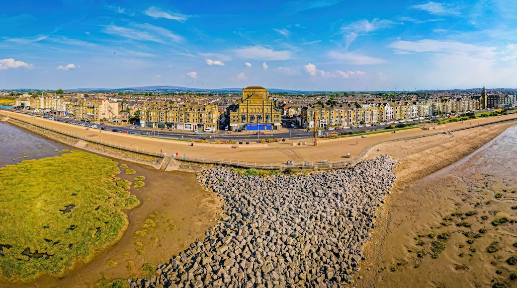 A coastal cityscape with a prominent historical building, a wide promenade, and a rocky shoreline.
