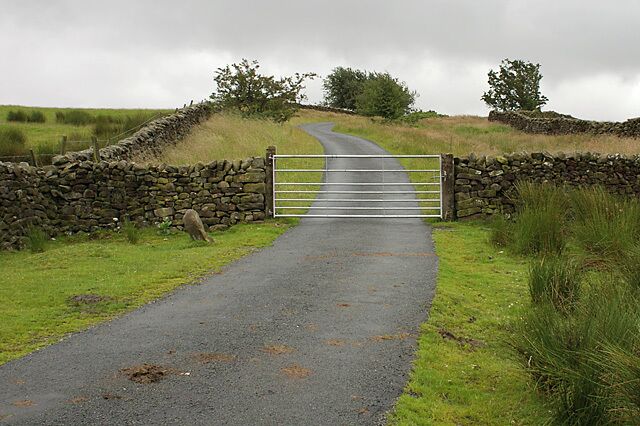 A rural road leading to a stone gate with a metal barrier.