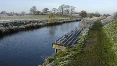 A river with a wooden bridge and frosty vegetation.