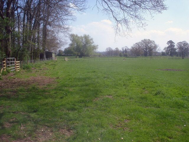 A grassy field with a fence, trees, and a small structure.