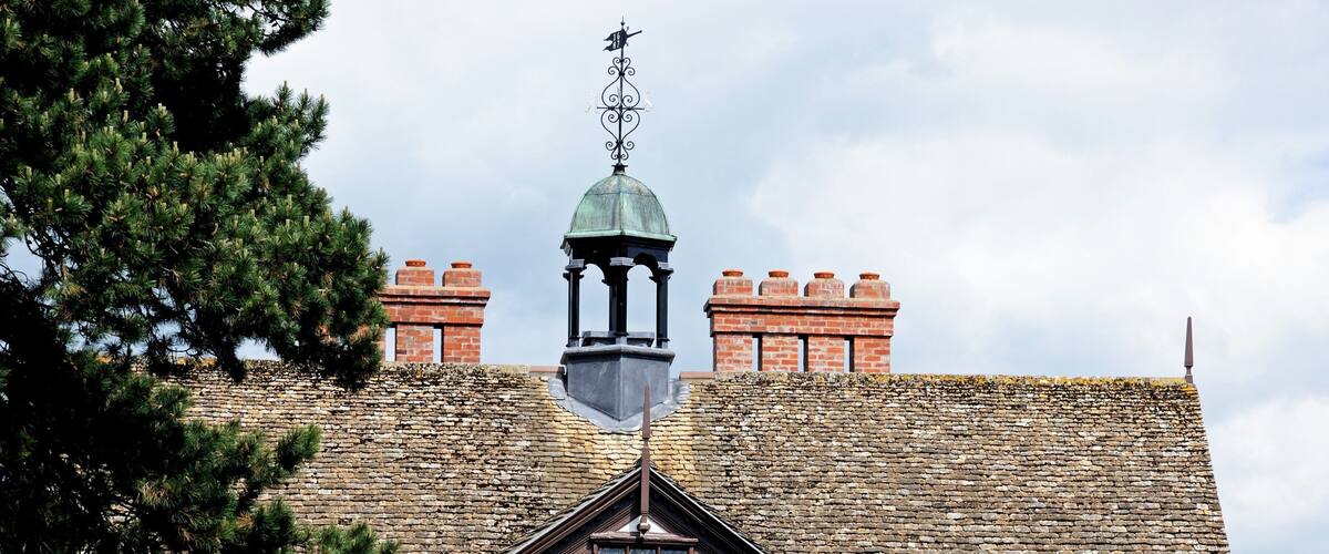 A traditional building with a stone roof, a weather vane, and a chimney.