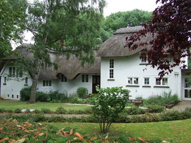 A white house with a thatched roof, surrounded by a well-maintained garden and a tree.