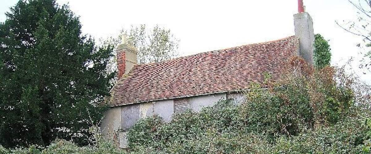 A house with a red-tiled roof, surrounded by dense green hedges and trees.