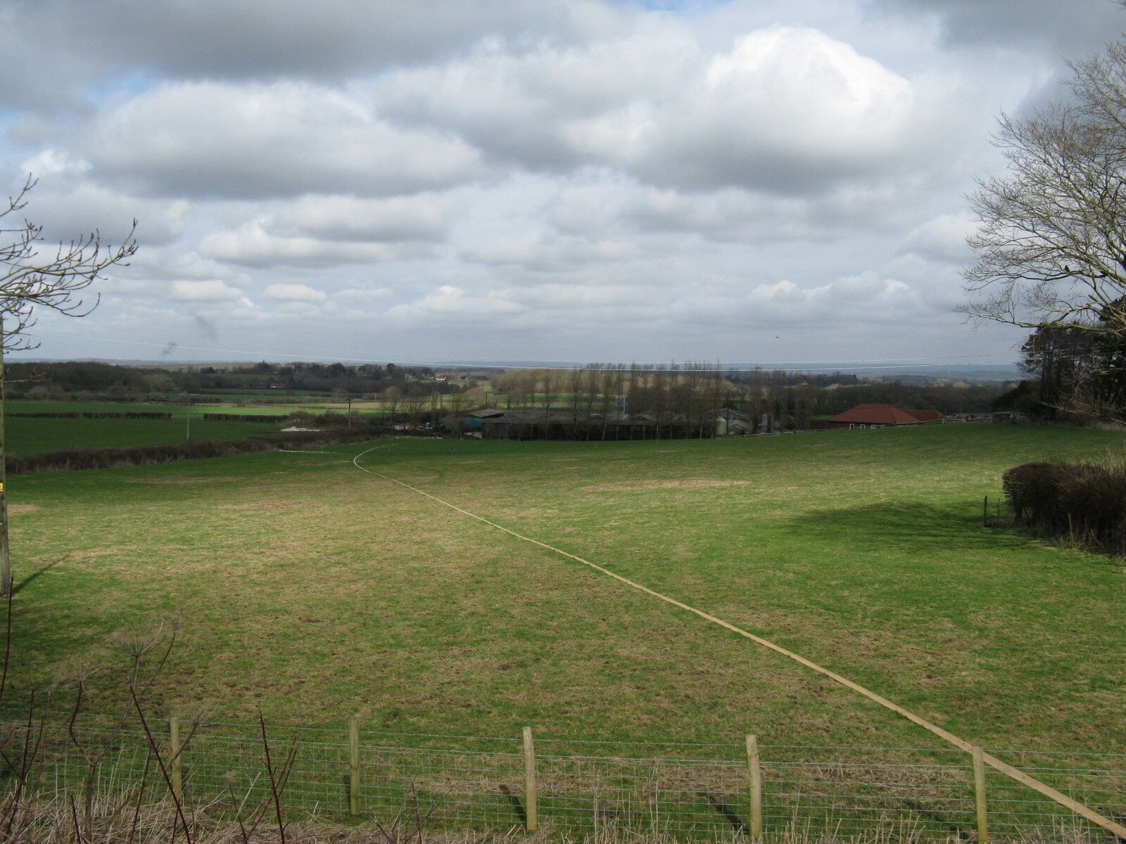 A rural landscape with a green field, a fence, and distant trees.