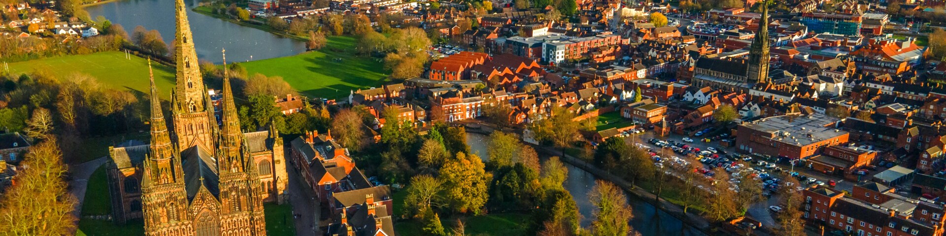 Lichfield Cathedral beside wide urban lake and green waterfront area