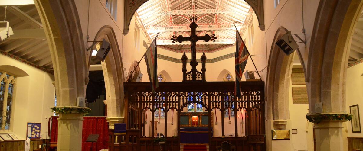 An interior of a church with wooden pews, a red carpet, and a stained glass window.