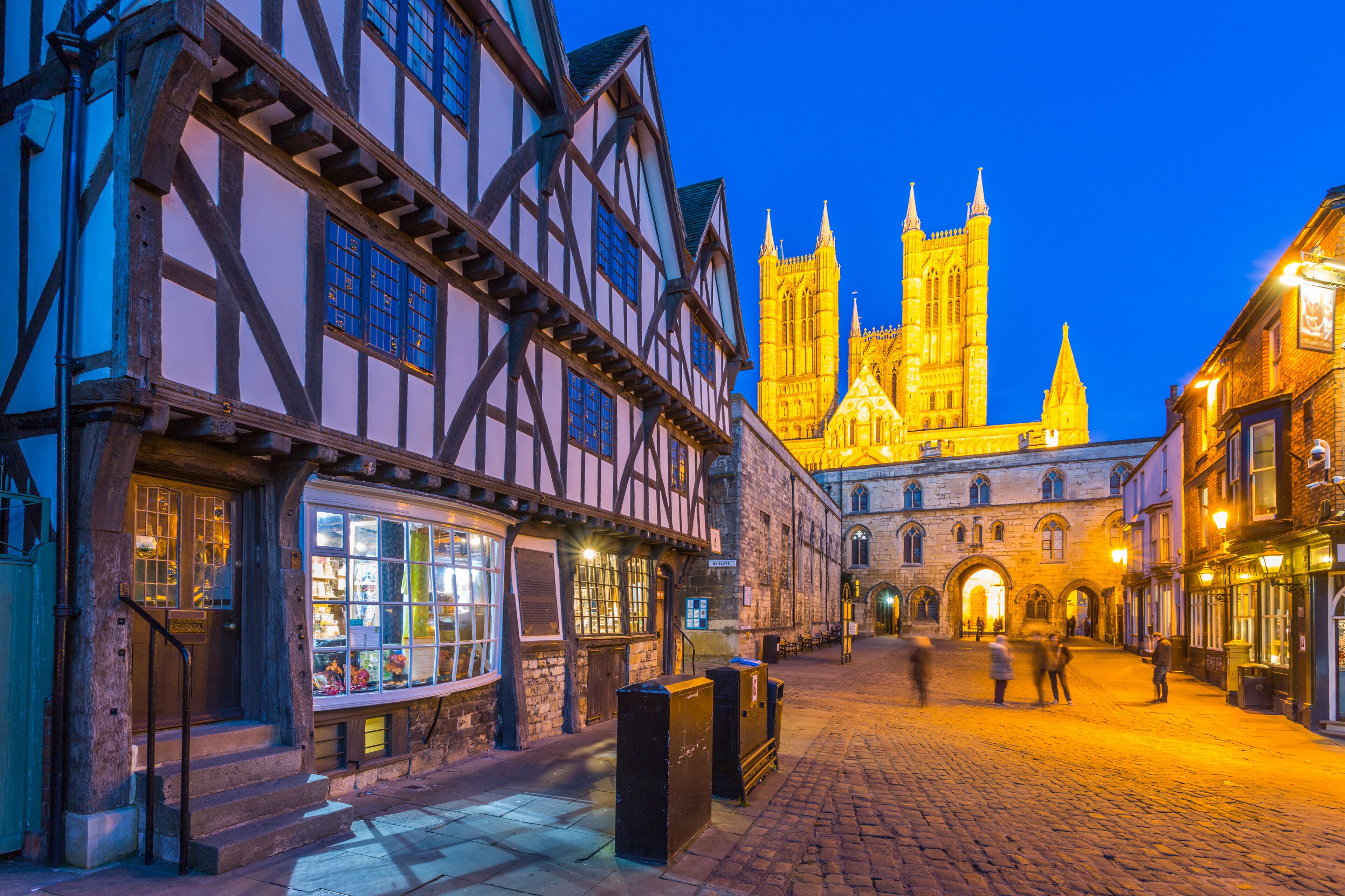 View of illuminated Lincoln Cathedral viewed from Exchequer Gate with timbered architecture of Visitors Centre at dusk, Lincoln, Lincolnshire, England